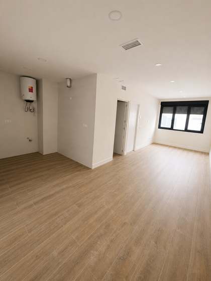 Salón-comedor diáfano con ventana a fachada y suelo de madera clara.
